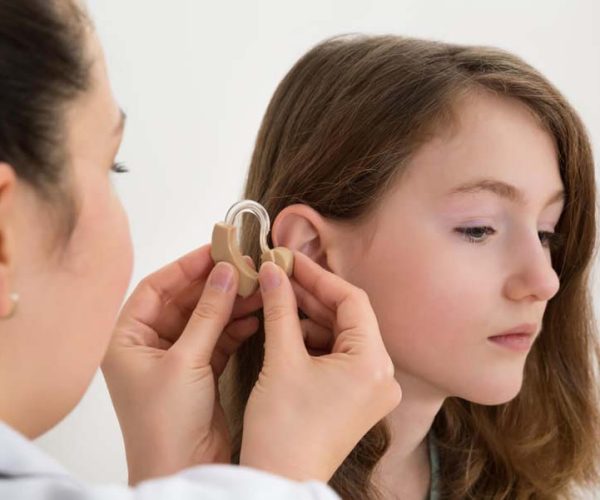 Audioprothésiste insérant une prothèse auditive dans l'oreille d'une fille
